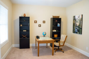 One single wooden office desk centered on room with two black bookcases flanking the desk. Artwork hung on wall behind office chair