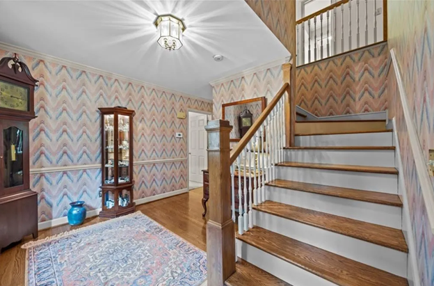 large entryway with busy wallpaper, grandfather clock and curio in hallway